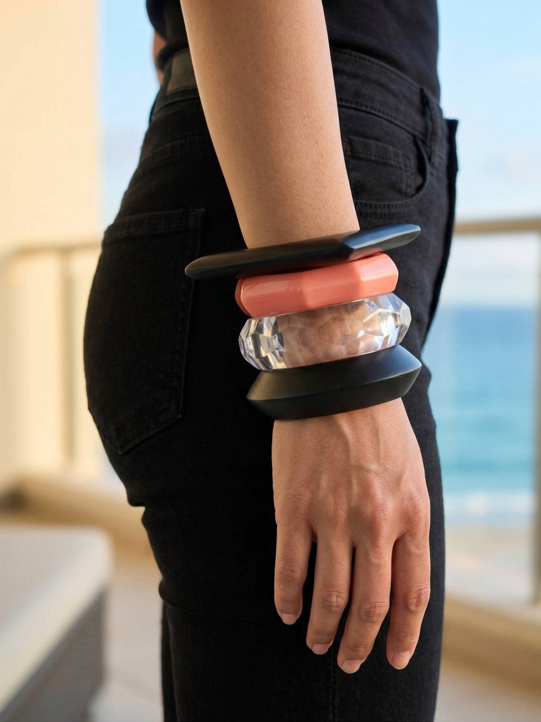 Side view of four stacked acrylic bangles on a wrist against an ocean balcony background