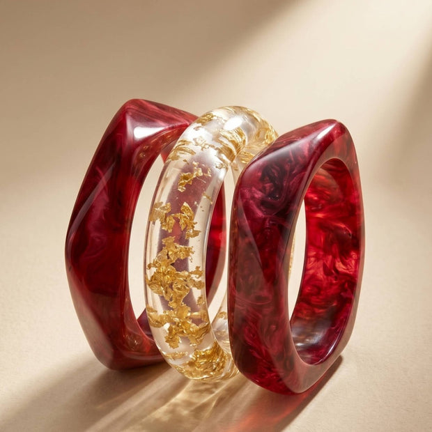 Set of three resin bangles displayed on a neutral surface, showing crimson marble swirl and transparent gold foil designs