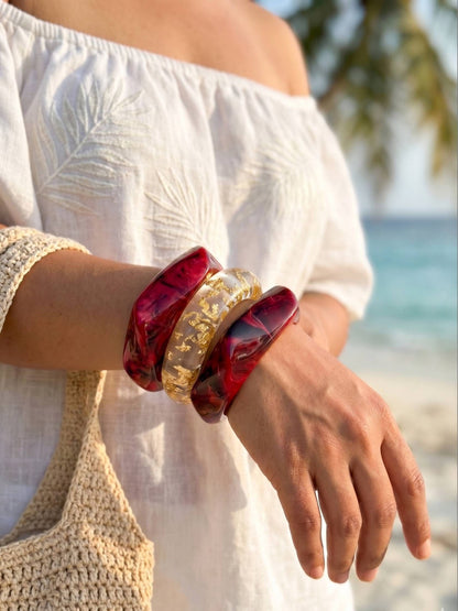Three resin bangles stacked on a wrist styled with a white off-shoulder top at a tropical beach setting
