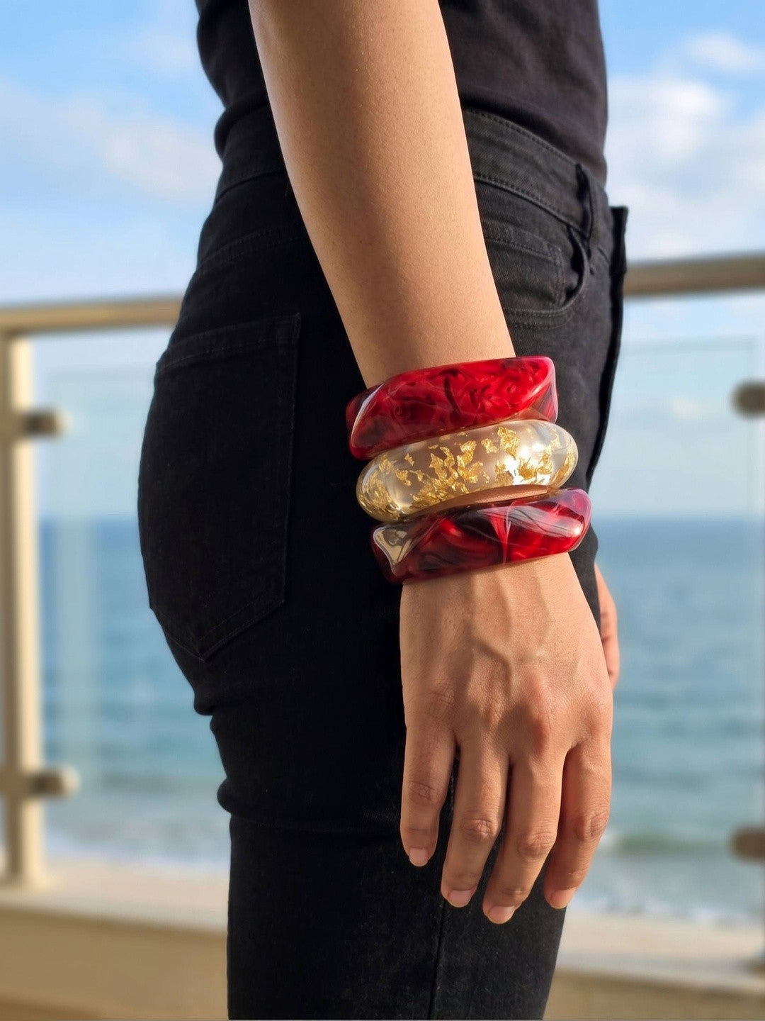 Stacked resin bangle set worn on a wrist against a black outfit with a blue ocean view in the background
