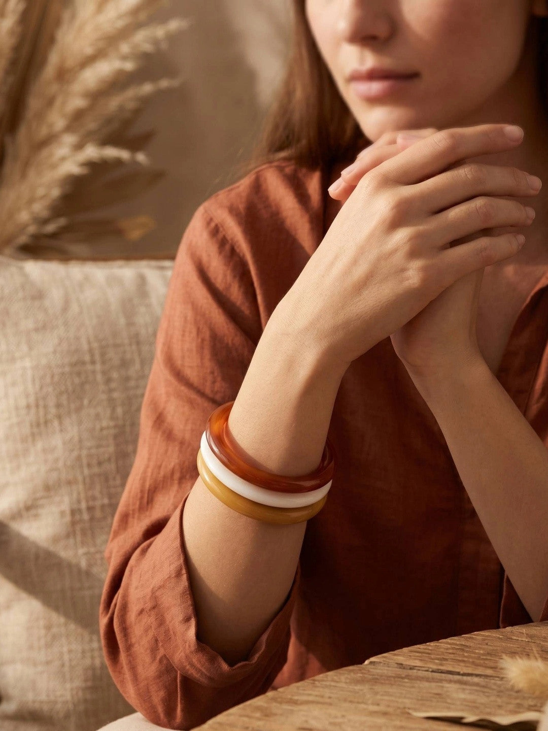 Woman wearing three stacked resin bangles in terracotta, ivory and mustard on her wrist with a rust linen shirt in warm light