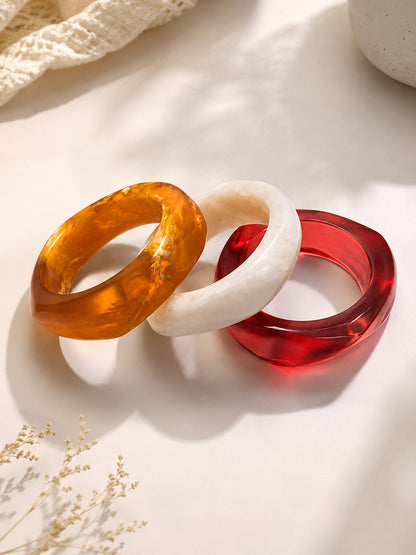 Three resin marble bangles in amber, white and red laid flat on a cream surface with dried flowers