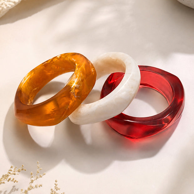 Three resin marble bangles in amber, white and red laid flat on a cream surface with dried flowers