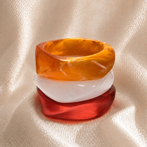 Amber, white and red chunky resin bangles stacked on top of each other on a cream fabric background