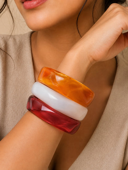 Three resin marble bangles stacked on a woman's wrist against a beige outfit