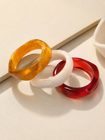 Three resin marble bangles in amber, white and red arranged leaning against a white prop on a cream surface