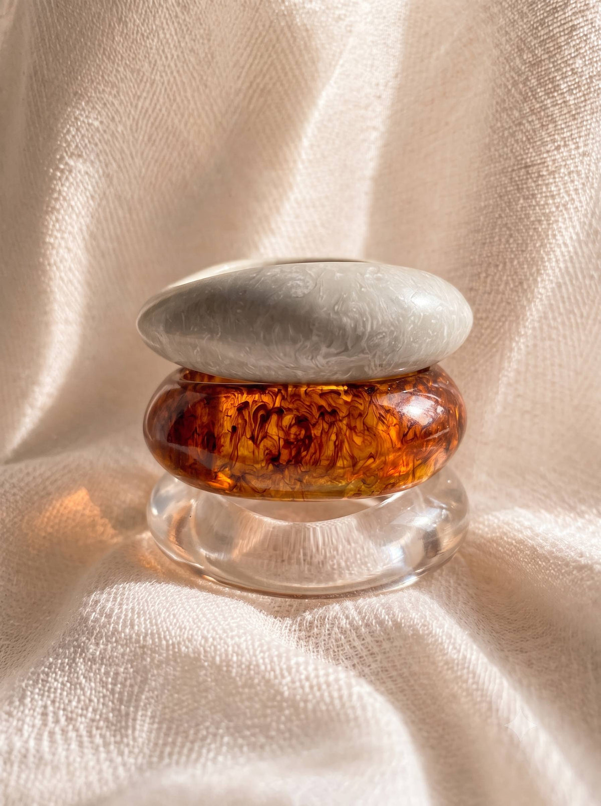 Three resin bangles stacked vertically showing marble white on top, amber tortoiseshell in centre and clear at base