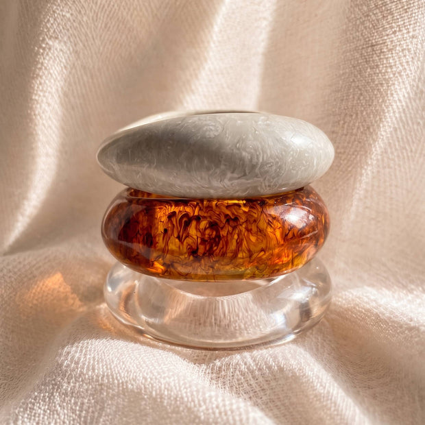 Three resin bangles stacked vertically showing marble white on top, amber tortoiseshell in centre and clear at base