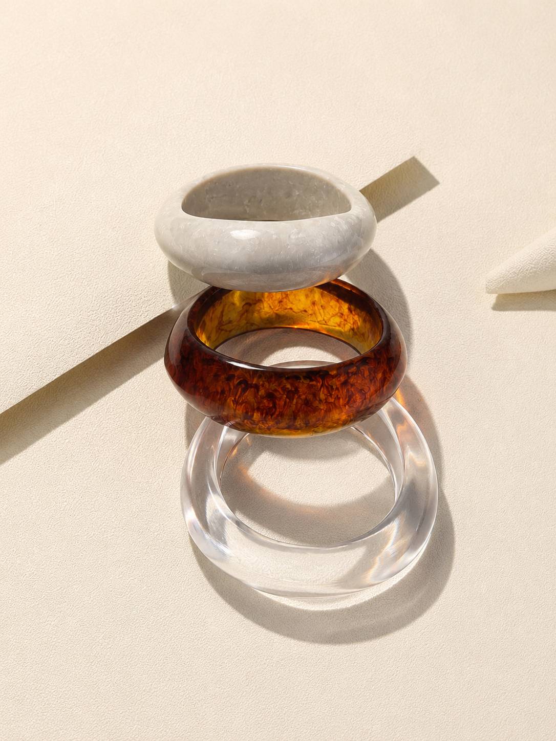 Marble white, amber and clear acrylic resin bangles stacked in a tower on a beige textured surface