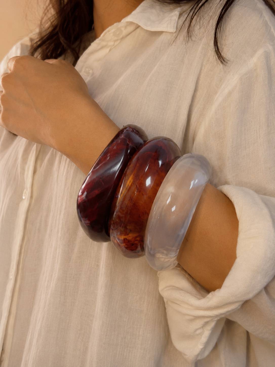 Woman wearing all three stacked resin marble bangles on her wrist with a white linen shirt