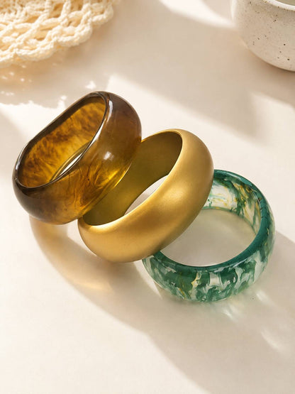 Amber marble, matte gold and green marble resin bangles lying flat and fanned out on a white surface