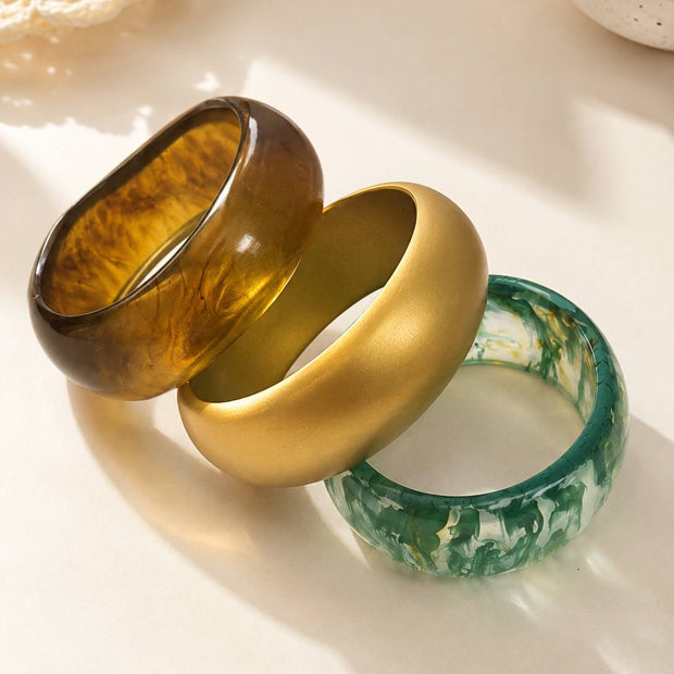 Amber marble, matte gold and green marble resin bangles lying flat and fanned out on a white surface