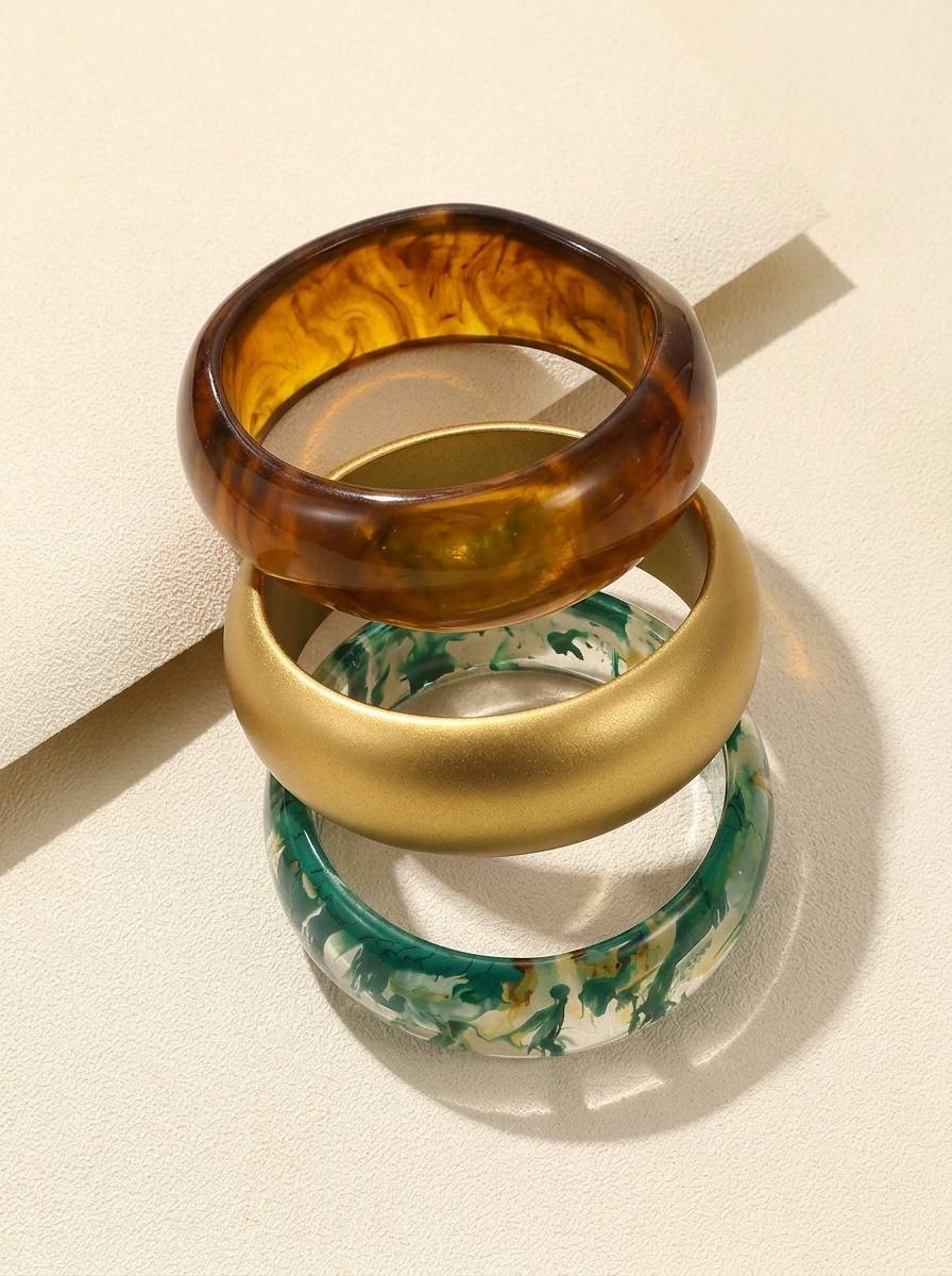 Three resin bangles stacked at an angle on a cream surface showing inner curves – amber, gold and green marble