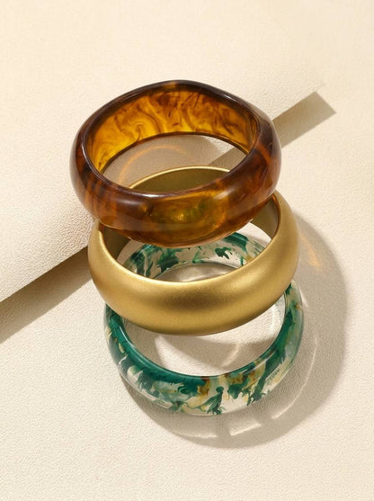 Three resin bangles stacked at an angle on a cream surface showing inner curves – amber, gold and green marble