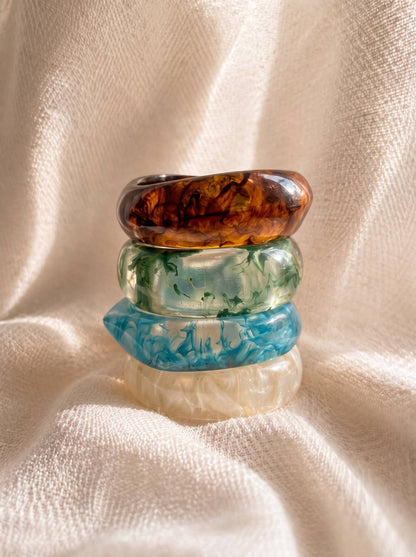 Four resin marble bangles stacked vertically on cream fabric showing amber, green, blue and ivory swirl patterns