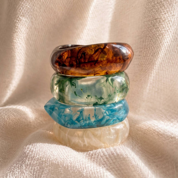 Four resin marble bangles stacked vertically on cream fabric showing amber, green, blue and ivory swirl patterns