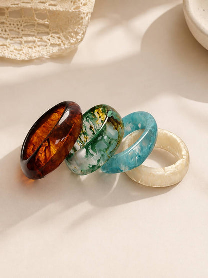 Four resin marble bangles arranged in a row on a light background with soft shadow highlights on each swirled design