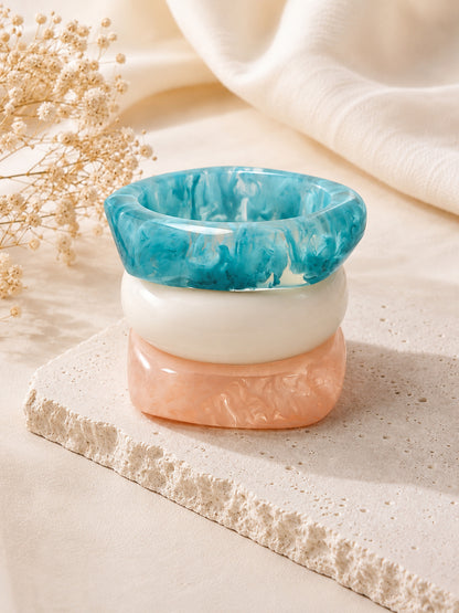 Three marble resin bangles stacked upright on a stone riser showing teal, white and peach layers from above