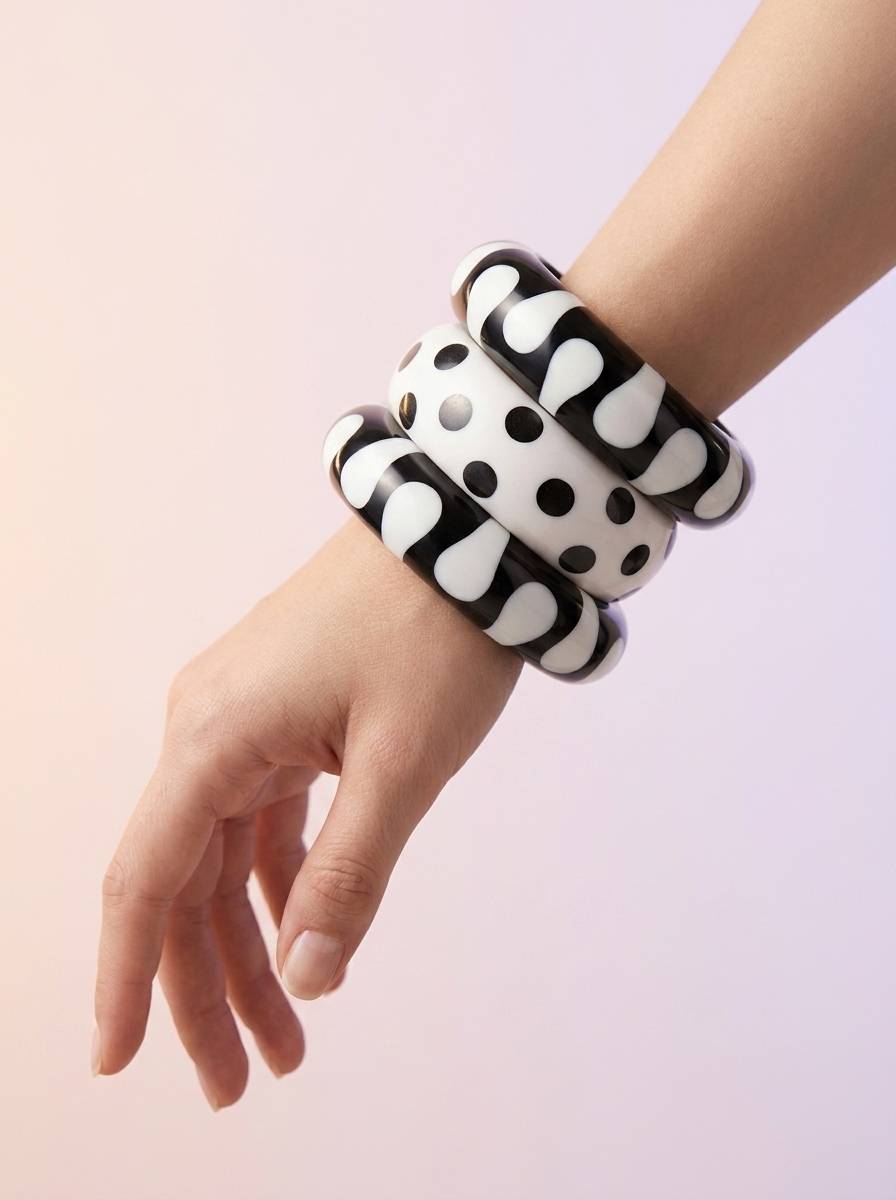 Black and white resin bangles stacked on a woman's wrist showing abstract blob and polka dot patterns against a soft pink background