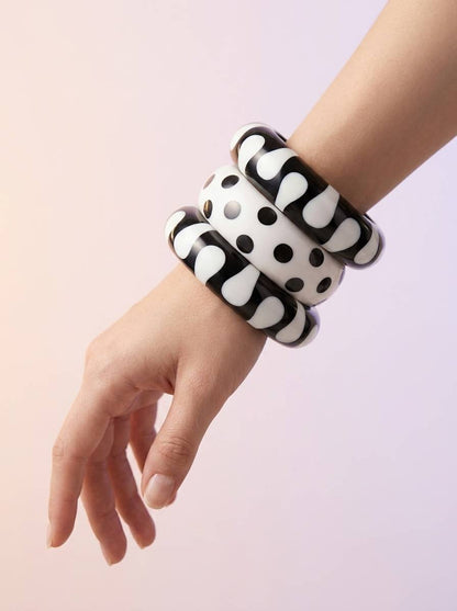 Black and white resin bangles stacked on a woman's wrist showing abstract blob and polka dot patterns against a soft pink background
