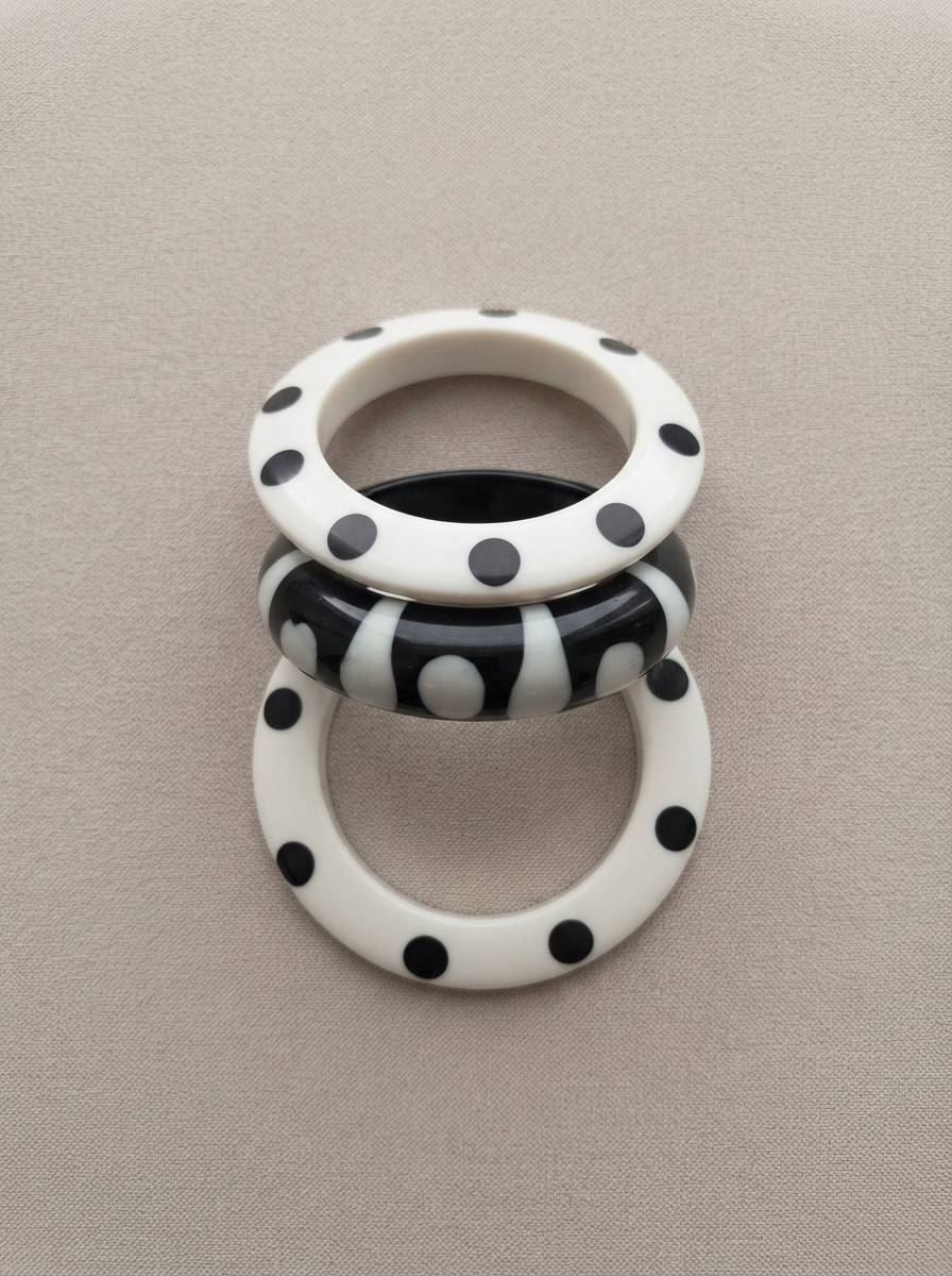 Three polka dot resin bangles laid flat on a grey fabric surface showing dot and stripe patterns clearly from above