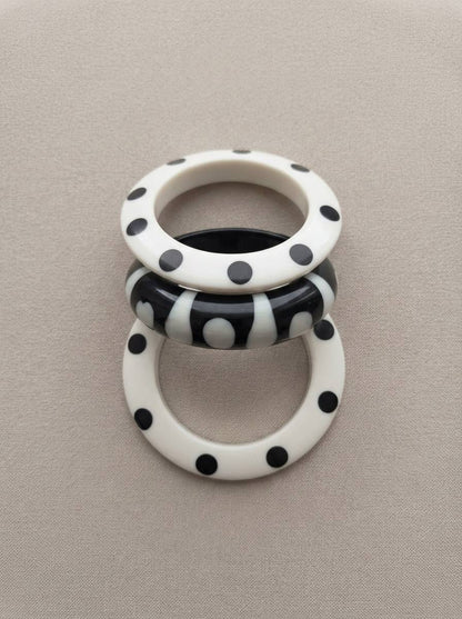 Three polka dot resin bangles laid flat on a grey fabric surface showing dot and stripe patterns clearly from above