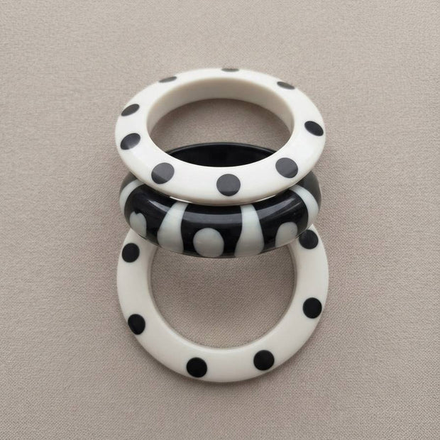 Three polka dot resin bangles laid flat on a grey fabric surface showing dot and stripe patterns clearly from above