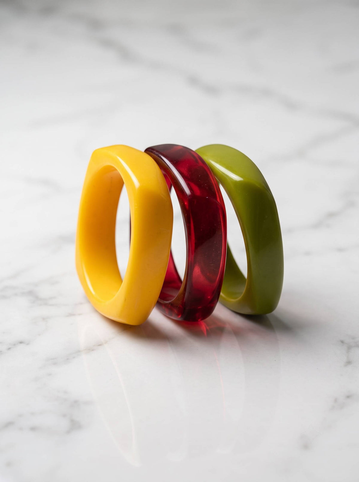 Yellow, translucent red, and olive green resin bangles stacked together on a white marble surface