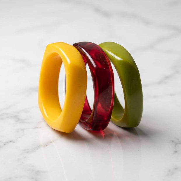 Yellow, translucent red, and olive green resin bangles stacked together on a white marble surface