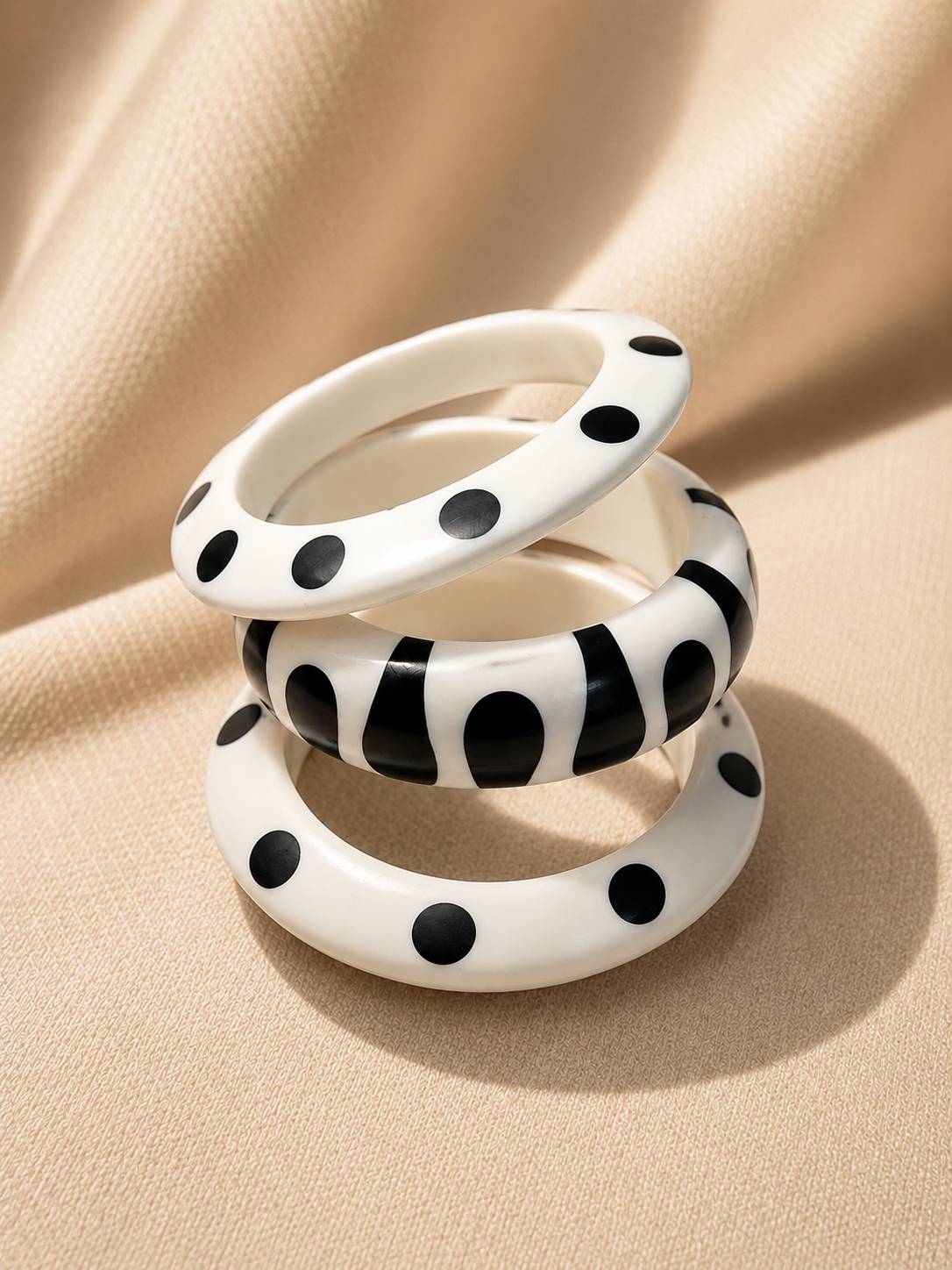 Three white resin bangles with black polka dot and abstract print patterns stacked on cream fabric