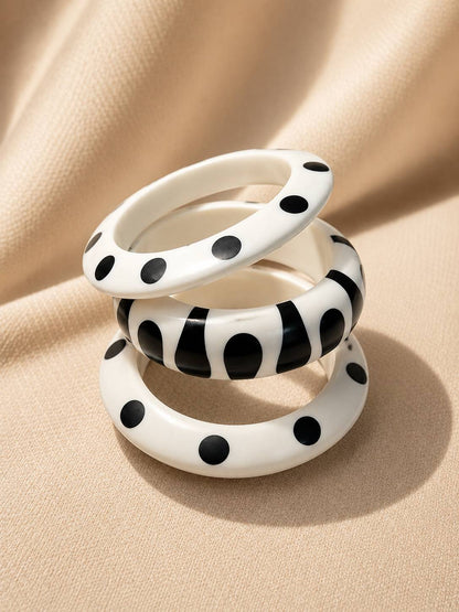Three white resin bangles with black polka dot and abstract print patterns stacked on cream fabric