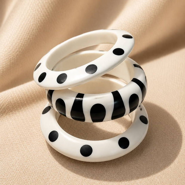 Three white resin bangles with black polka dot and abstract print patterns stacked on cream fabric