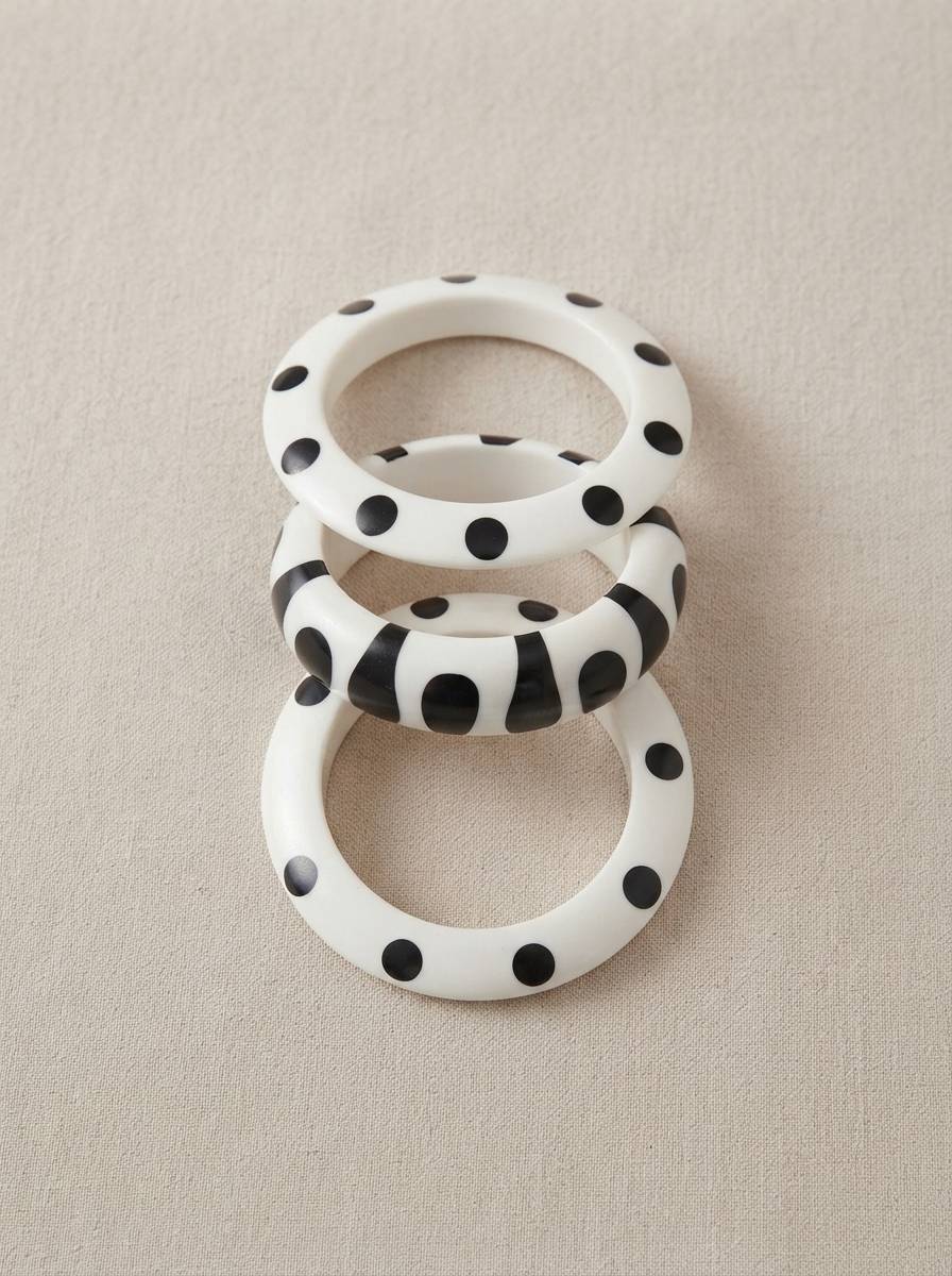 Set of three black and white resin bangles laid flat — two polka dot and one stripe print — on a linen surface