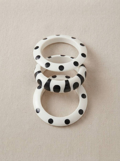 Set of three black and white resin bangles laid flat — two polka dot and one stripe print — on a linen surface