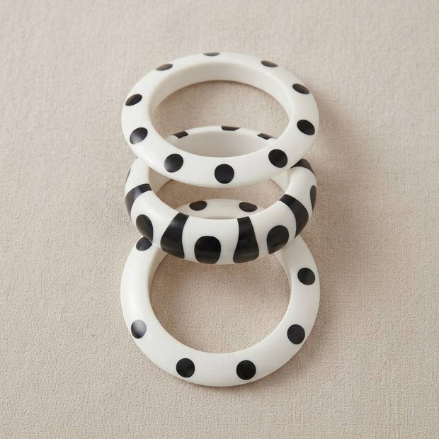 Set of three black and white resin bangles laid flat — two polka dot and one stripe print — on a linen surface