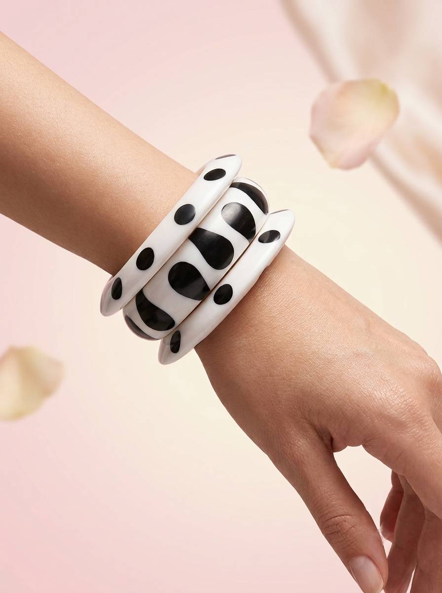 Three black and white printed resin bangles worn together on a woman's wrist against a pink floral background
