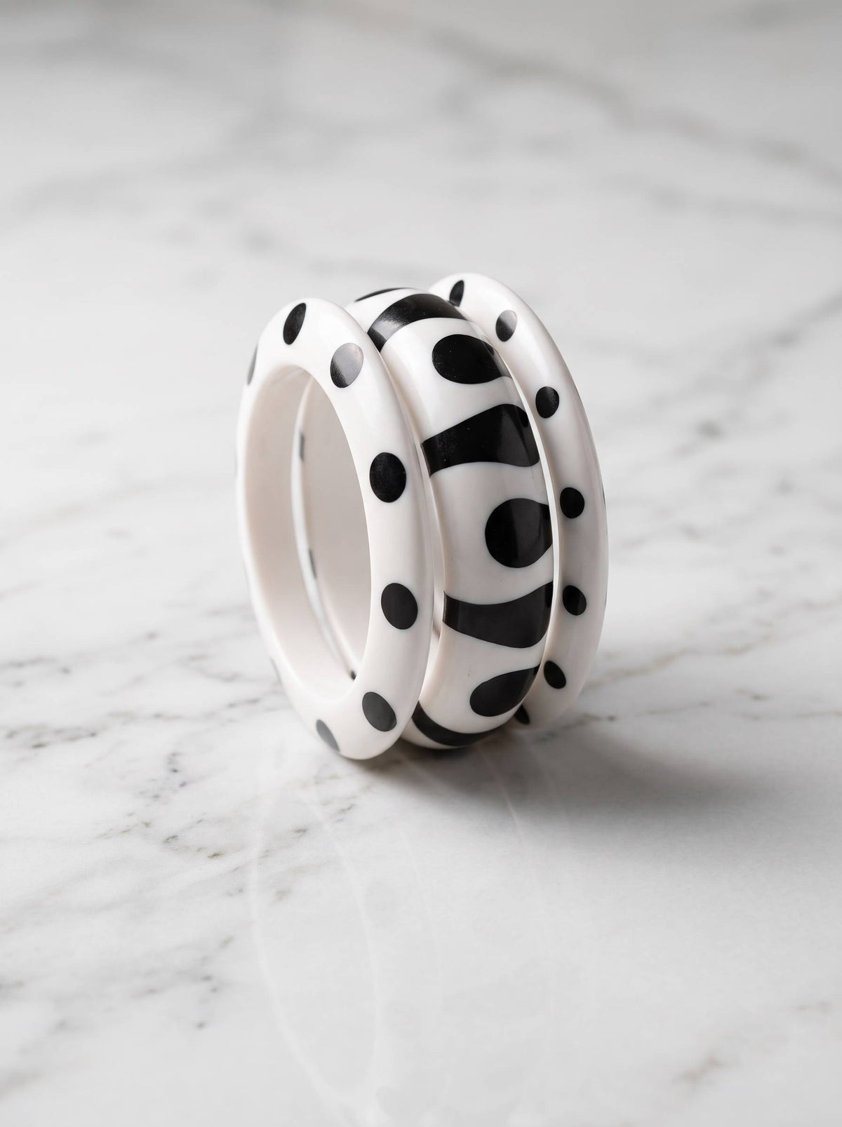 Two polka dot and one abstract black and white resin bangle stacked upright on white marble surface