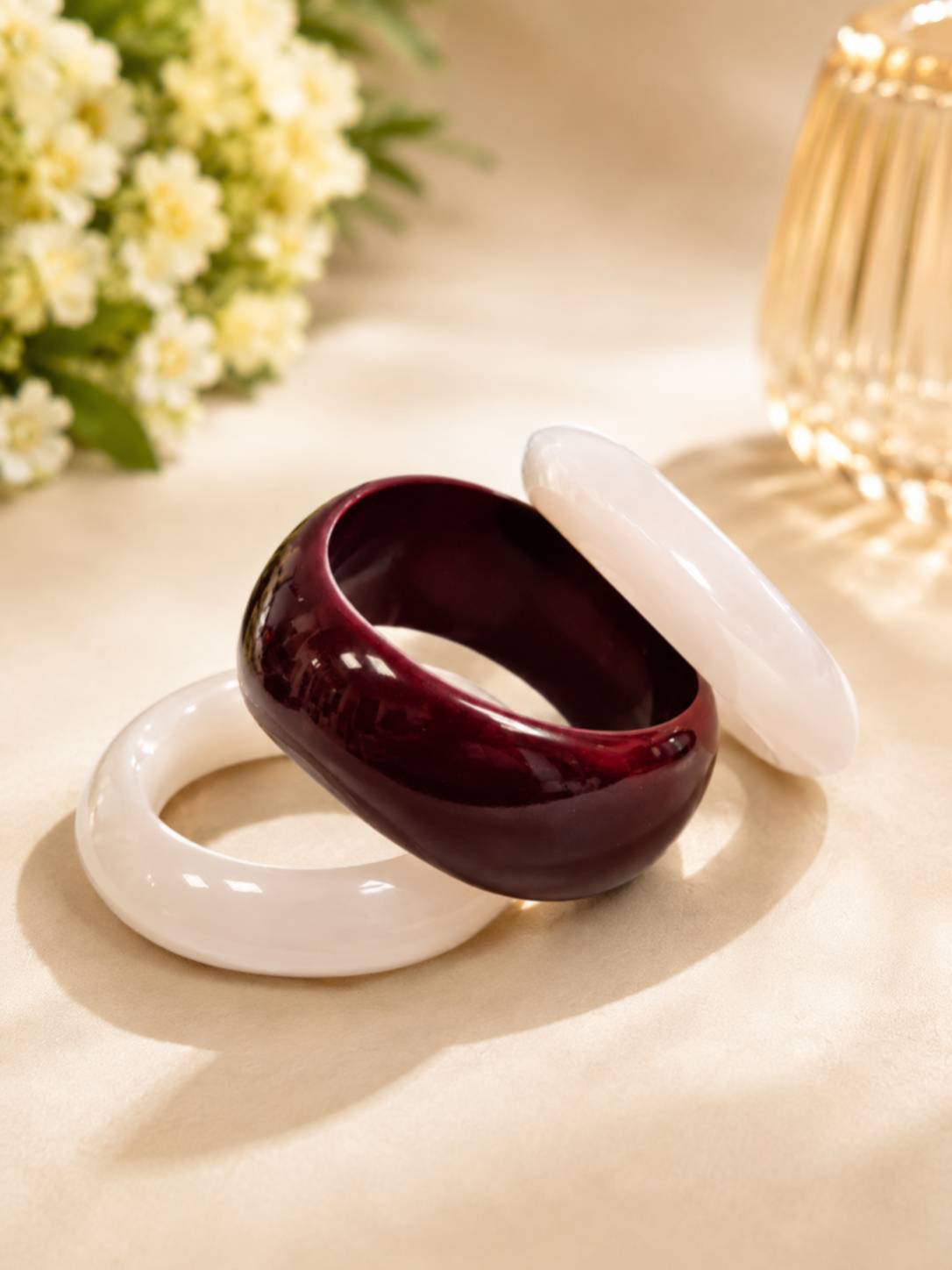 Three resin bangles arranged on satin with white flowers and gold geometric candle holder in background
