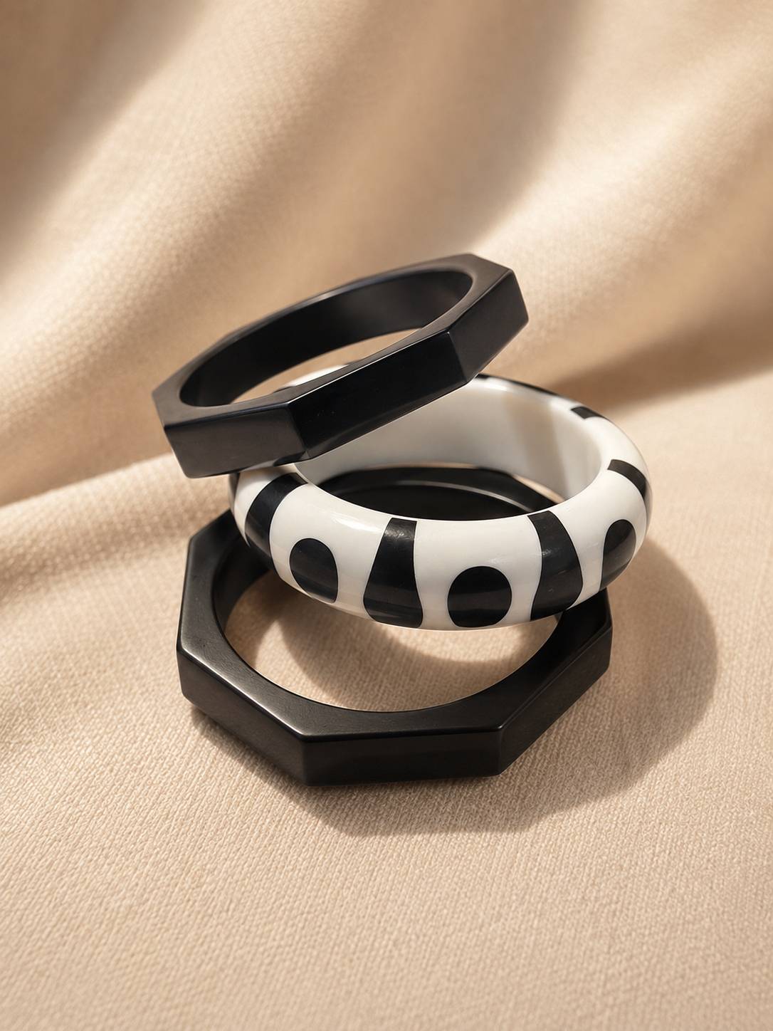 Three black and white resin bangles stacked on beige fabric, two octagonal black and one round monochrome printed