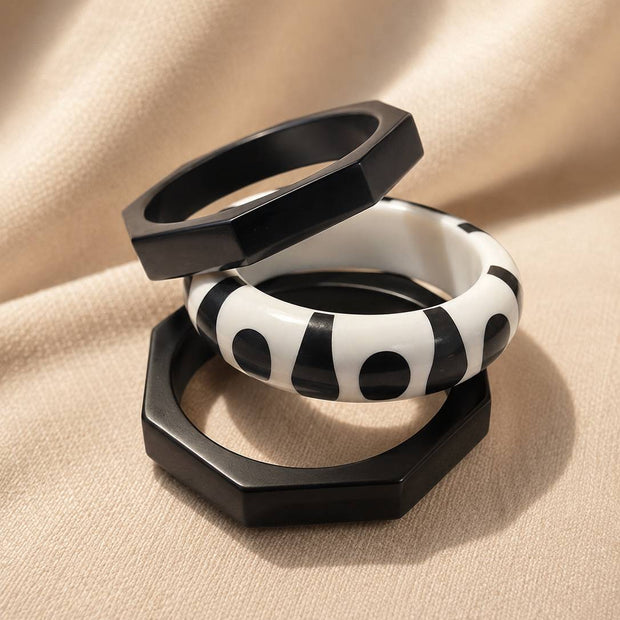Three black and white resin bangles stacked on beige fabric, two octagonal black and one round monochrome printed