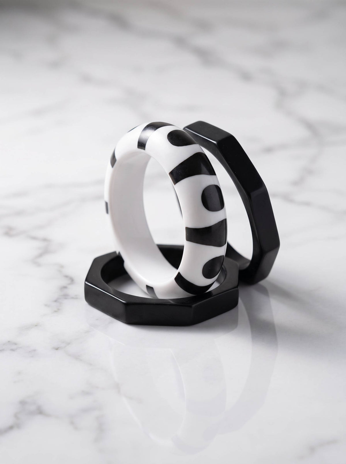 Two octagonal matte-black resin bangles and one round printed bangle arranged on white marble surface