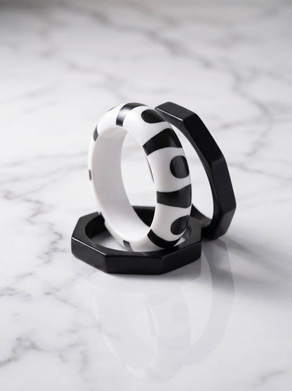 Two octagonal matte-black resin bangles and one round printed bangle arranged on white marble surface