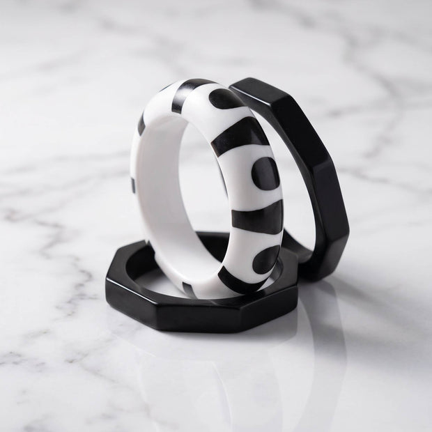 Two octagonal matte-black resin bangles and one round printed bangle arranged on white marble surface