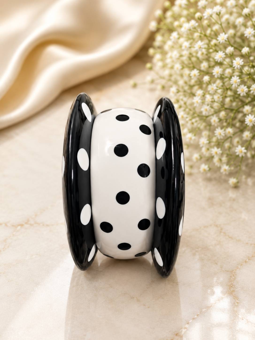 Black and white polka dot resin bangle set standing upright on a marble surface showing the chunky rounded profile and glossy finish