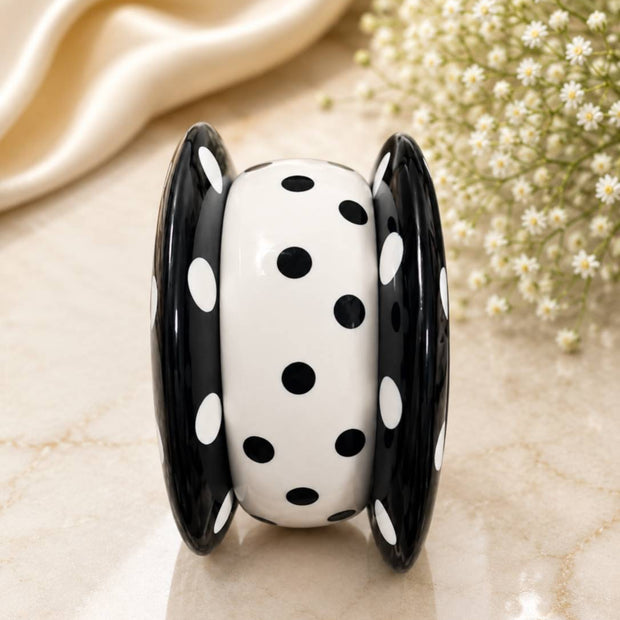 Black and white polka dot resin bangle set standing upright on a marble surface showing the chunky rounded profile and glossy finish