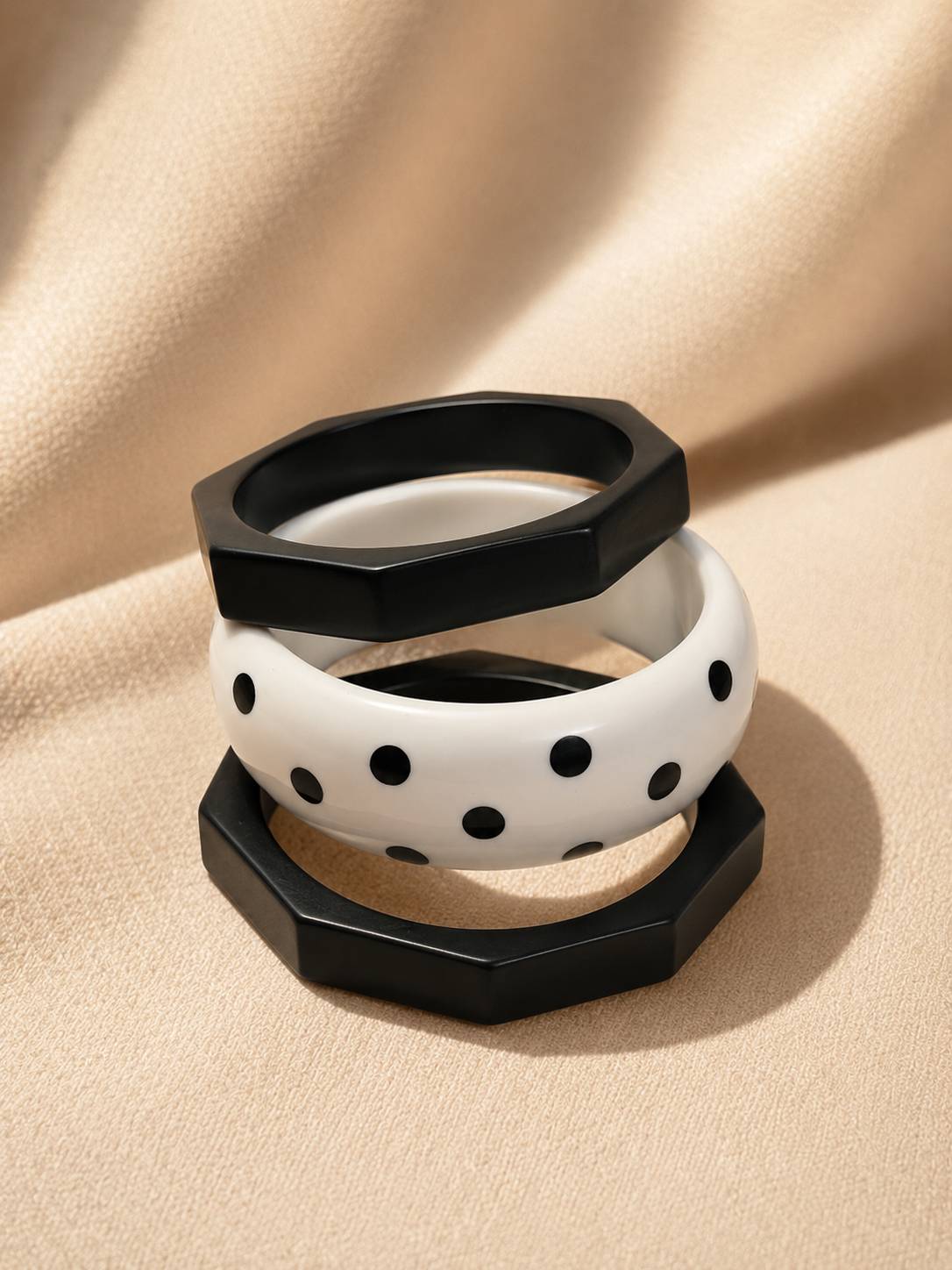 Three resin bangles stacked on beige fabric — two black octagonal and one white polka-dot bangle