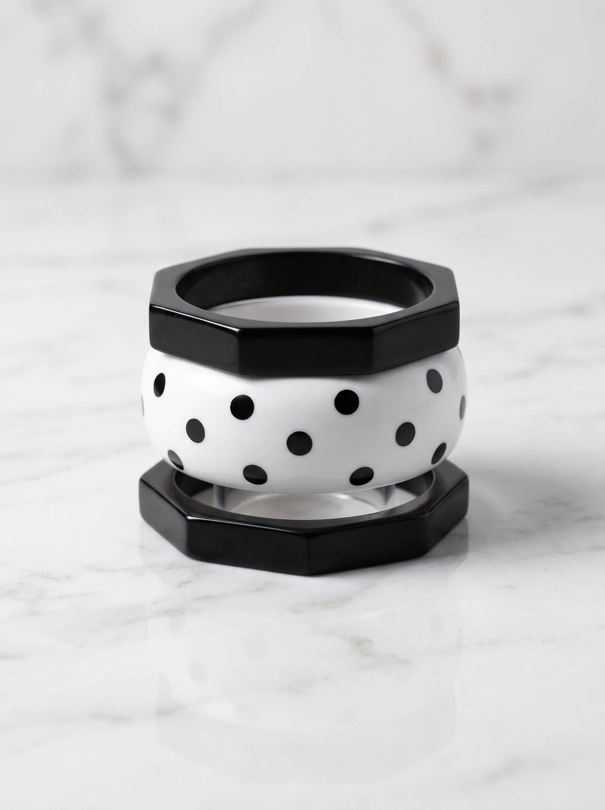 Black octagonal bangle on top and bottom sandwiching a white polka-dot resin bangle on marble surface