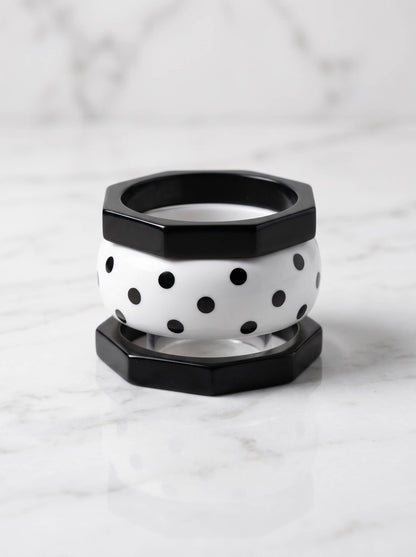 Black octagonal bangle on top and bottom sandwiching a white polka-dot resin bangle on marble surface