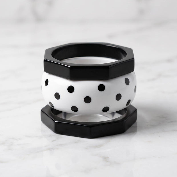 Black octagonal bangle on top and bottom sandwiching a white polka-dot resin bangle on marble surface