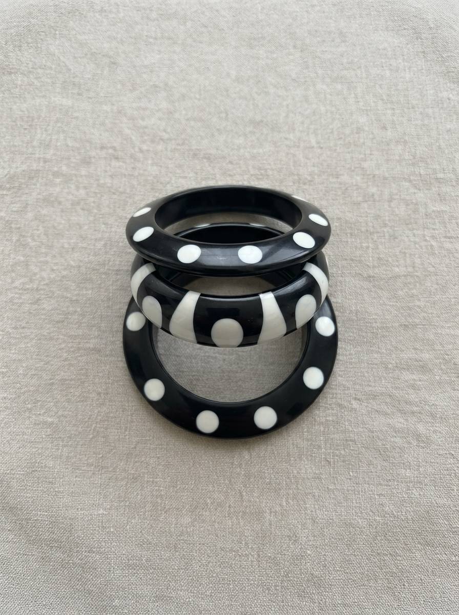 Set of three black resin bangles with white polka dots and stripe pattern stacked upright on a grey linen background